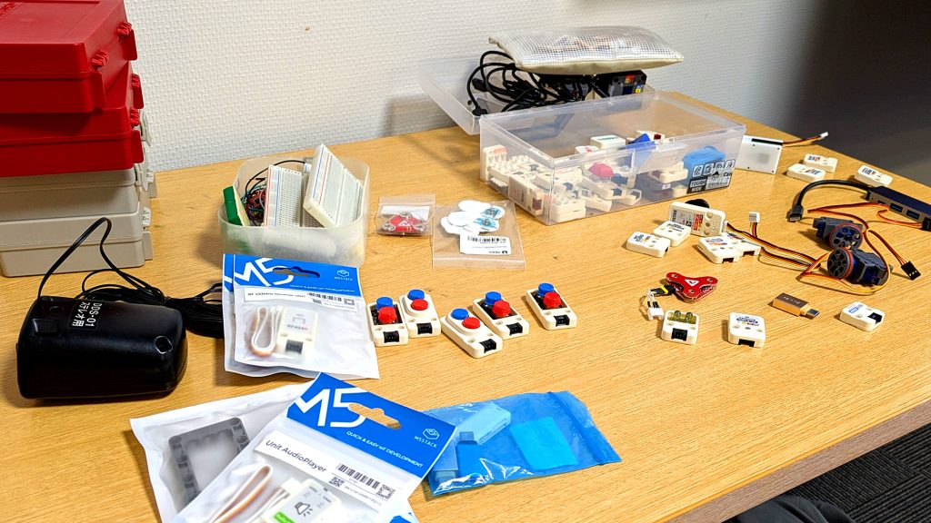 予備のM5Stack、様々なセンサー、接続ケーブルが机に散りばめられている様子